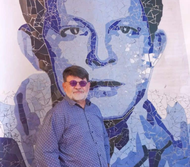 La foto muestra al artista Ricardo Flecha, posando frente a un mural de José Asunción Flores.